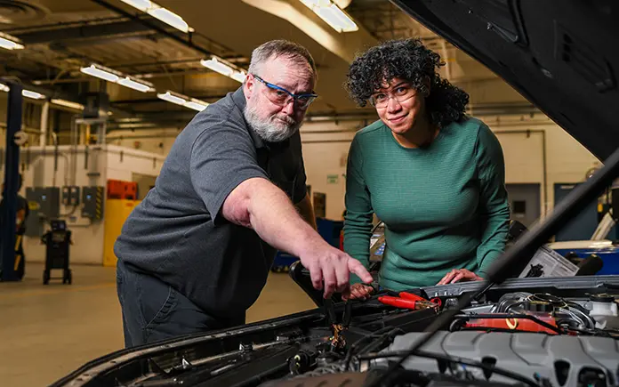 Automotive instructor and student work on a car's engine.