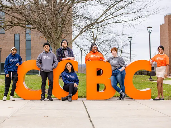 Six students stand around orange letters that spell CCBC