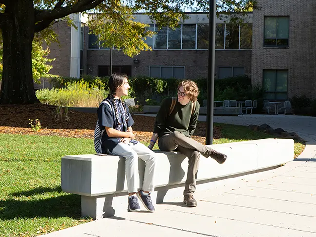 Two students sitting next to each other chatting outside