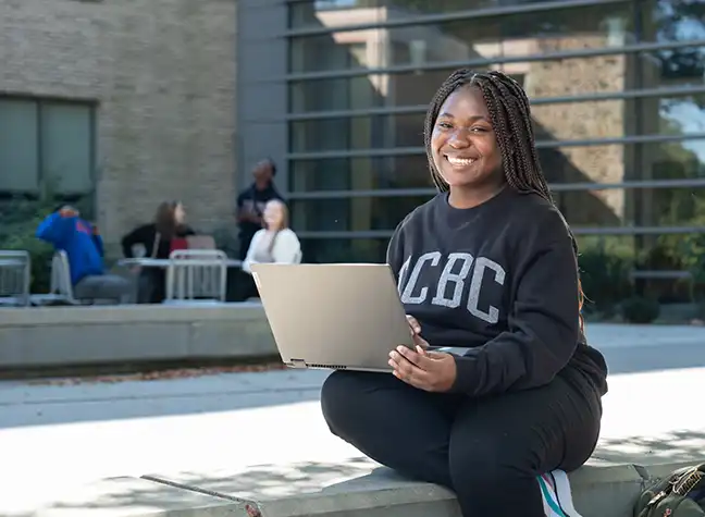 CCBC student on her laptop sitting in front of the Math and Science building