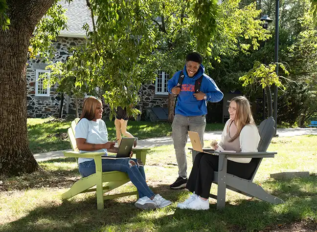 Group of CCBC student hangout out under trees on campus