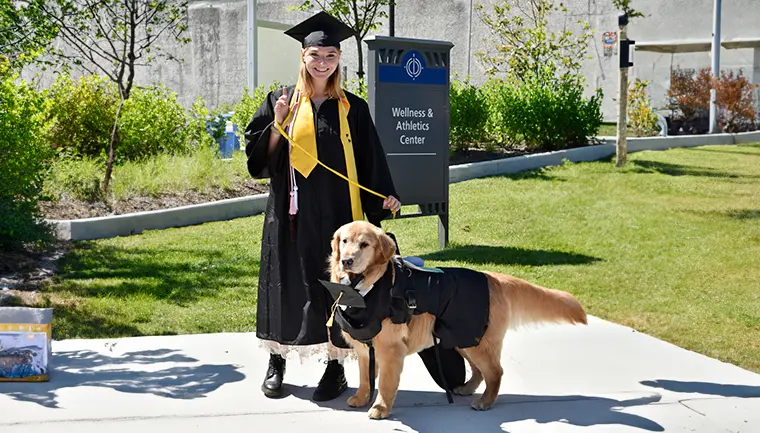 A graduating student in her regalia standing with her service dog