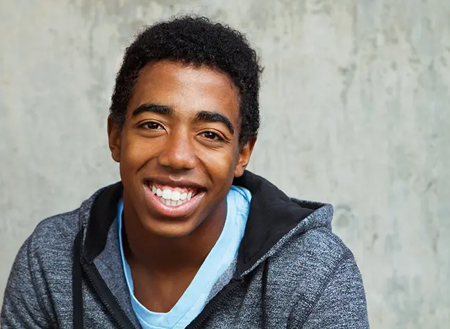 A close up portrait of a teenage boy smiling at the camera in a gray sweater.