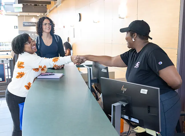 A student and a staff member shaking hands over a desk.