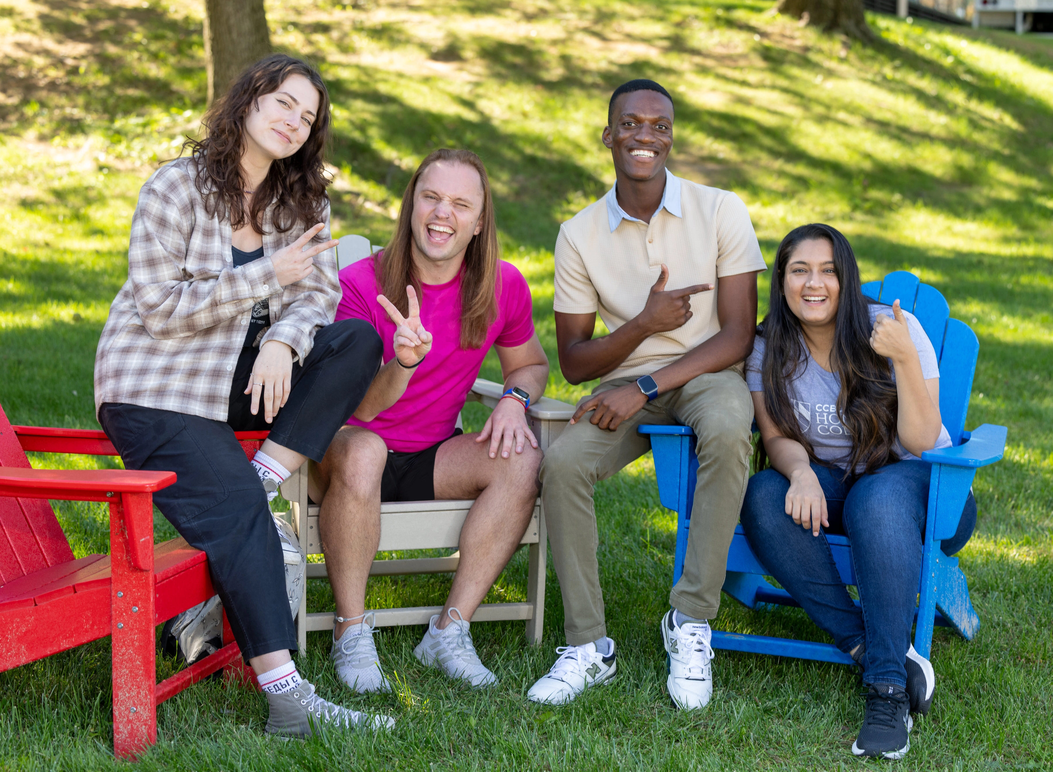 Four students sitting in colorful lawn chairs on a sunny day.